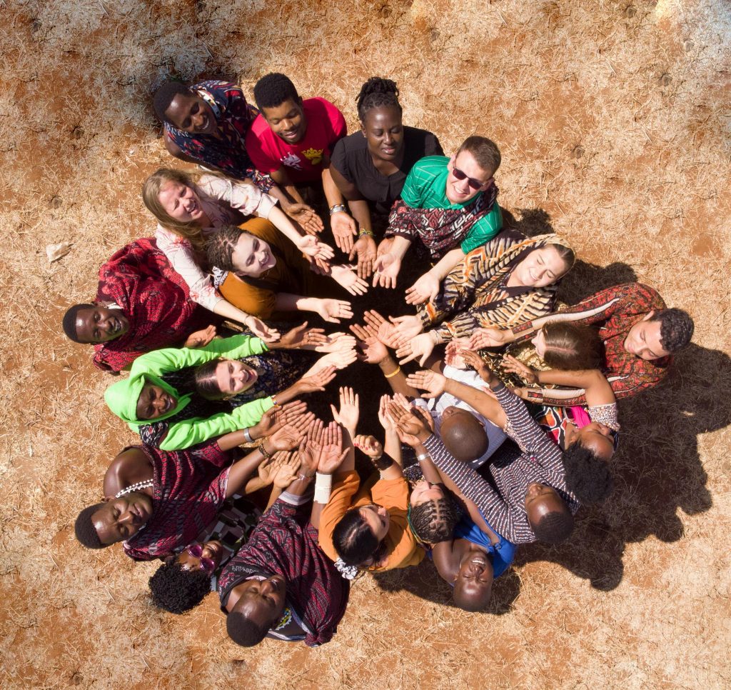 Home Aerial view of a diverse group in Tanzania symbolizing unity and teamwork by joining hands.